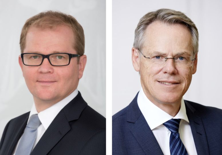 The picture shows portraits of the two Managing Directors of the Austrian Treasury. The left side of the picture shows the Managing Director of the division “Markets”, Markus Stix. He wears thick black glasses and a dark blue suit, a white shirt and a light blue tie. The right side of the picture shows the Managing Director of the division “Risk Management & Operations”, Walter Joestl. He wears a dark blue suit, a white shirt and a dark blue-striped tie as well as frameless glasses.